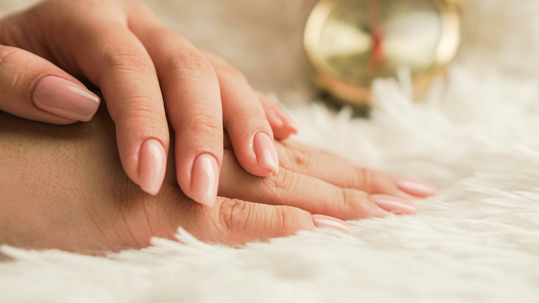 Soft pink manicure resting on white fur